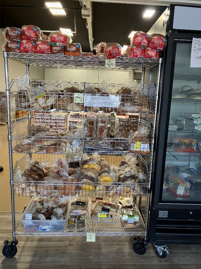 A metal cart with shelves holding bakery items, such as bread and bagels.